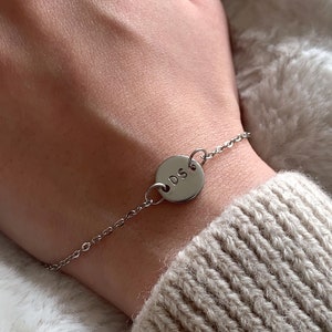 Könnte beinhalten: Ein silbernes Kettenarmband mit einem runden Anhänger, auf dem die Initialen "D.S." eingraviert sind.
