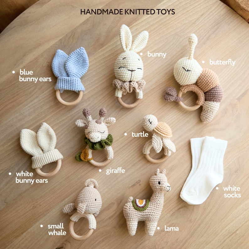 May include: Handmade knitted toys for babies, including a blue bunny, white bunny, giraffe, turtle, llama, small whale, butterfly, and a pair of white socks. The toys are all crocheted and have wooden rings for teething.