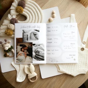 An open pregnancy journal with photos and handwritten details. The book includes a photo of a baby's hand, a couple, and a baby's foot. A crocheted giraffe rattle, bunny ear rattle, and a pair of socks are also visible.