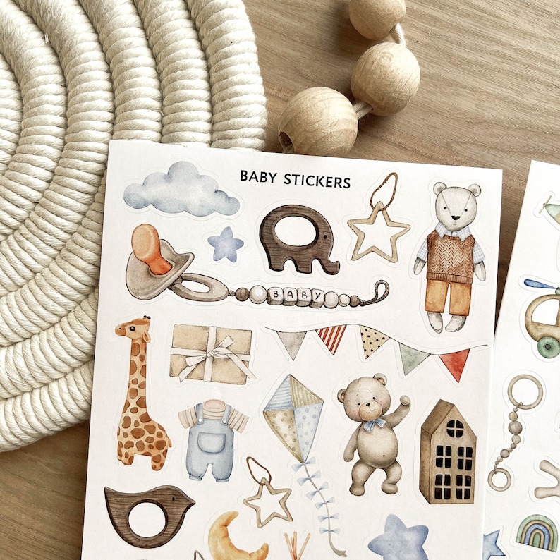 May include: A sheet of baby stickers with watercolor illustrations. Designs include a pacifier, elephant, giraffe, teddy bear, and a kite. The stickers are in soft pastel colors, with the words "BABY STICKERS" at the top.