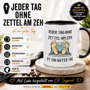Op de afbeelding: Een witte keramische mok met een zwarte handgreep en binnenrand. De mok is voorzien van een afbeelding van twee voeten met een teenlabel en de Duitse tekst 'Jeder Tag ohne Zettel am Zeh ist ein guter Tag' op de voorzijde van de mok.