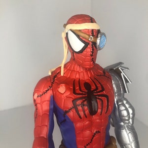 May include: A red, blue, and black Spider-Man action figure with a steampunk aesthetic. The figure features a metallic arm, goggles, and stitched details. A black spider emblem is on the chest, and a brown belt is around the waist.