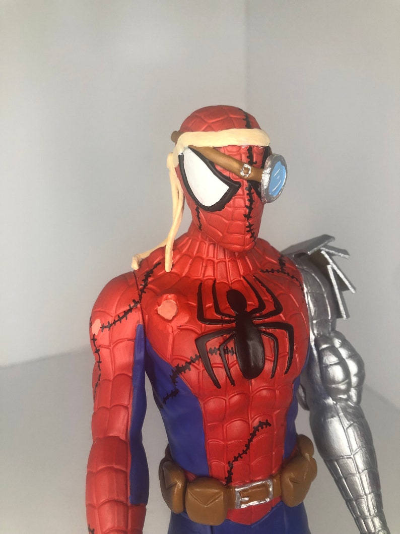 May include: A red, blue, and black Spider-Man action figure with a steampunk aesthetic. The figure features a metallic arm, goggles, and stitched details. A black spider emblem is on the chest, and a brown belt is around the waist.