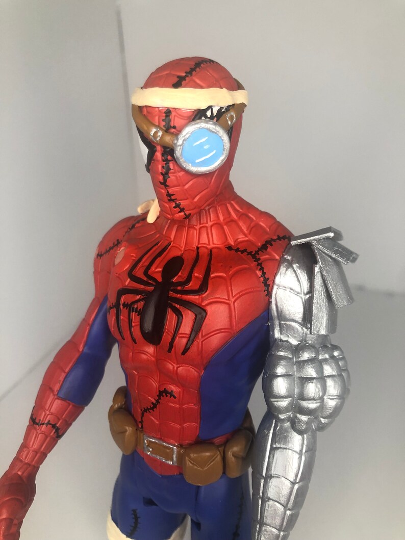 May include: A red, blue, and black Spider-Man action figure with a steampunk-inspired design. The figure features a metallic arm, goggles, and stitched details. The figure has a black spider emblem on the chest and a brown utility belt.