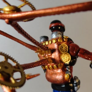 May include: A steampunk-inspired figurine with a copper and gold color scheme. The figure has a red torso, silver head, and is adorned with gears and mechanical elements. The design incorporates intricate details and a vintage aesthetic.