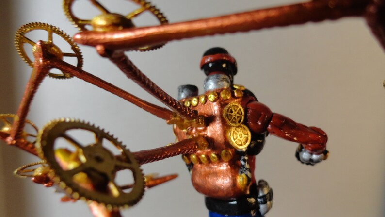 May include: A steampunk-inspired figurine with a copper and gold color scheme. The figure has a red torso, silver head, and is adorned with gears and mechanical elements. The design incorporates intricate details and a vintage aesthetic.