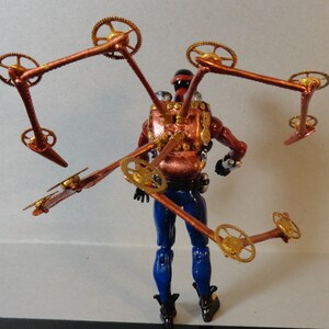 May include: A steampunk-themed action figure with a red and copper-colored torso, blue pants, and black boots. The figure has multiple articulated copper arms with gold-colored gears attached. The figure is posed against a plain background.