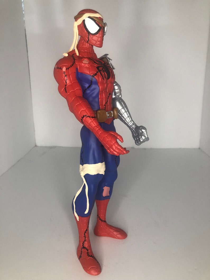 May include: A red, blue, and silver Spider-Man action figure with a unique design. The figure features a robotic arm, stitched seams, and bandages. The figure has a brown belt and a black spider emblem on the chest.
