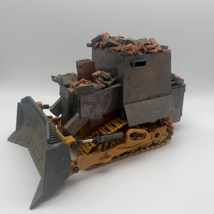 May include: A yellow toy bulldozer with a black blade and a grey metal cab. The cab is filled with small, orange and brown toy bricks.