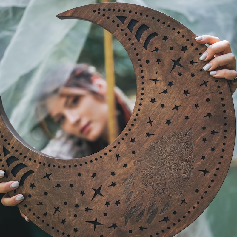 May include: A crescent moon-shaped wooden wall hanging with a dark brown finish. The moon features cut-out stars, a decorative owl design, and a series of small holes along the edge. The design is held by a person.