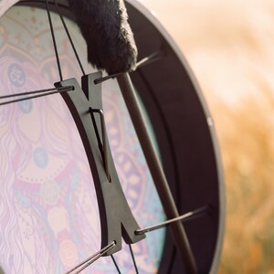 May include: A black frame drum with a colourful mandala design and a black wooden handle. The drum is strung with black cords.