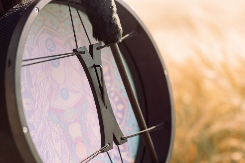 May include: A black frame drum with a colourful mandala design and a black wooden handle. The drum is strung with black cords.