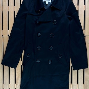 May include: A black double-breasted trench coat with a large collar and a button closure. The coat has a label that reads "H&M" on the inside collar.