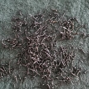 May include: A large collection of silver-toned metal earring hooks, each featuring a curved wire, a small decorative bead, and a coiled spring detail at the base, designed for jewellery making and crafting projects with a standard fishhook style.