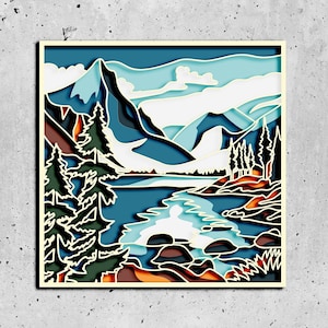 Puede incluir: Una obra de arte recortada en papel que representa un paisaje de montaña con un río que fluye a través de él. Las montañas son azules y blancas, el río es azul y los árboles son verdes. El cielo es azul claro con nubes blancas.