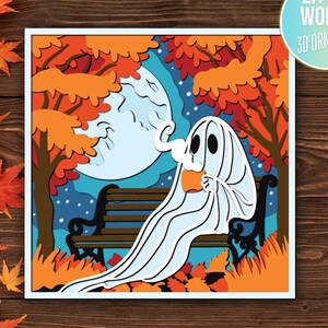 May include: A layered paper art piece featuring a ghost sitting on a park bench, holding a mug, with a full moon and autumn foliage in the background. The artwork is framed and includes the text "LITTLE WORLD 3D ORNAMENTS".