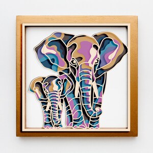 May include: A framed paper art piece showing a mother elephant and calf. The artwork is in a gold-coloured wooden frame. The elephants are in shades of purple, blue, and brown, creating a colourful and artistic representation. The artwork is a layered design.