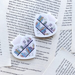 May include: Two heart-shaped stickers with a bookshelf design. The stickers feature a white background with pink and green floral accents. The books on the shelves are in various colors, including blue, pink, green, and yellow. The text on one sticker reads "Read".