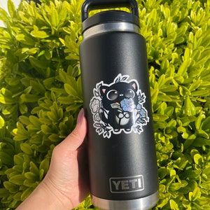 May include: A black Yeti water bottle with a sticker of a black cat holding flowers. The sticker has a holographic finish.
