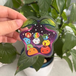 May include: A clear sticker with a star-shaped design featuring cartoon characters and gifts. The sticker has a dark purple and blue background with white stars. The characters are in various colors, including blue, orange, and yellow.