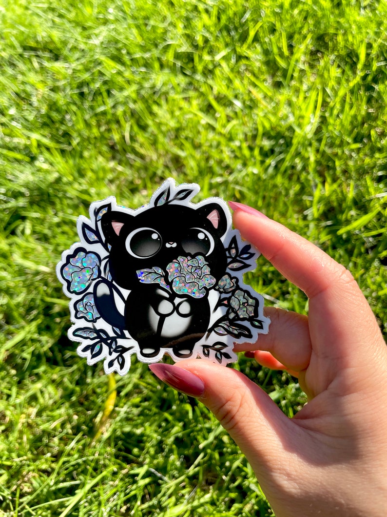 May include: A black and white sticker of a cartoon cat holding a bouquet of iridescent flowers. The cat has large eyes and a small mouth. The flowers are surrounded by leaves and vines.