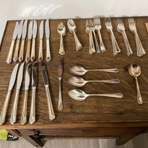 May include: A set of silverware, including forks, knives, and spoons, laid out on a wooden table. The silverware is made of polished silver and has a traditional design.