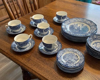 May include: A vintage blue and white china tea set, including teacups, saucers, plates, and bowls, displayed on a wooden table. The tableware features a detailed landscape pattern. The set includes multiple teacups, saucers, plates, and bowls.