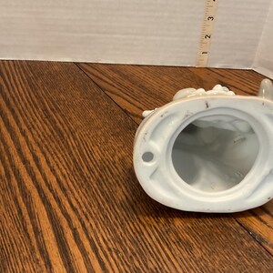 以下が含まれることがあります： 白磁の置物で、内側は水色です。置物には取っ手があり、花の装飾が施されています。ベースは楕円形です。置物の高さは約7.6cmです。