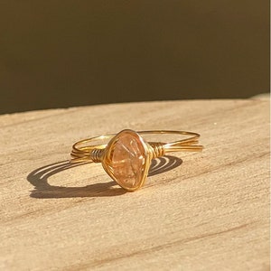 May include: A gold wire wrapped ring with a light pink and clear gemstone.