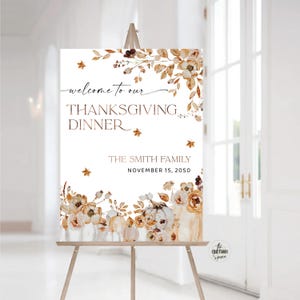 Puede incluir: Un cartel de bienvenida blanco con un diseño de acuarela de hojas de otoño y calabazas. El texto dice "Bienvenido a nuestra cena de Acción de Gracias, La familia Smith, 15 de noviembre de 2050".