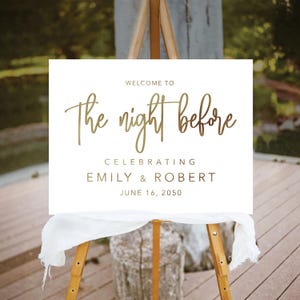 May include: White sign with gold lettering that reads "Welcome to the night before celebrating Emily & Robert June 16, 2050".
