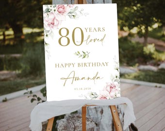 May include: White sign with gold lettering and pink floral illustrations. The sign reads "80 Years Loved Happy Birthday Amanda 05.18.2050".