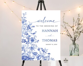 May include: A white wedding welcome sign with blue floral designs and birds. The text reads "Welcome to the wedding of Hannah and Thomas August 12, 2050".