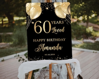 May include: A black sign with gold text and accents, displayed on a wooden easel. The sign reads "60 Years Loved, Happy Birthday Amanda" with gold balloon graphics. The date "05.18.2050" is also included.
