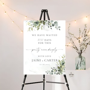 May include: A wedding welcome sign with a watercolour background featuring green leaves and branches. The sign reads "We have waited 1050 days for this party accordingly with love Jaimi & Carter 10.28.2023"