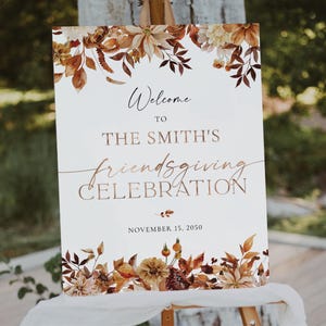 May include: Welcome to The Smith's Friendsgiving Celebration sign with a white background and fall-themed floral border. The text is in a copper-colored font. The date is November 15, 2050.
