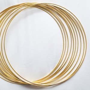 Puede incluir: Un conjunto de diez aros de metal de color dorado, dispuestos en círculo, con el aro más grande en la parte posterior y el aro más pequeño en la parte delantera.