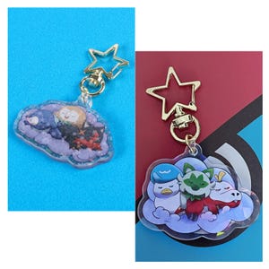 May include: Two clear acrylic keychains with gold star-shaped clasps. Each keychain features a cloud with a group of cartoon characters sleeping on it. The first keychain features a blue, white, and black character, a white character, and a black character. The second keychain features a blue and white character, a green and white character, and a red and white character.