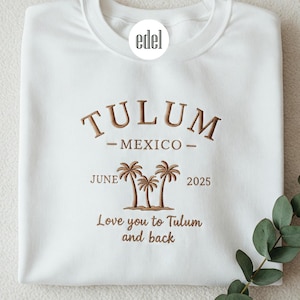 Puede incluir: Sudadera blanca con texto bordado en marrón que dice "Tulum - México - Junio 2025" y "Te quiero en Tulum y de regreso". El texto está rodeado por un gráfico de palmeras.