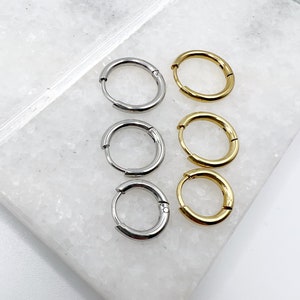 May include: A set of six hoop earrings, three silver and three gold, on a white marble surface.