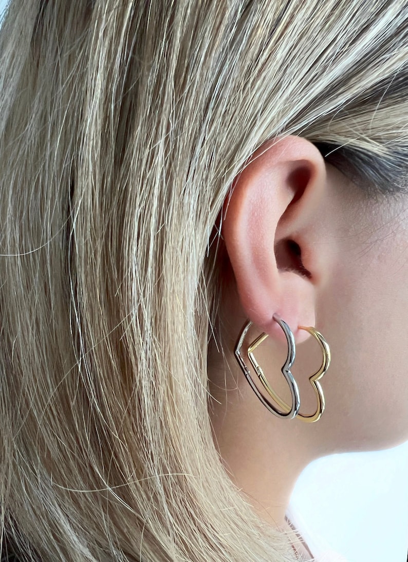 Peut inclure: Une paire de boucles d'oreilles cr&eacute;oles en forme de c&oelig;ur. Les boucles d'oreilles sont en deux m&eacute;taux diff&eacute;rents, l'un en or et l'autre en argent. Les boucles d'oreilles sont port&eacute;es &agrave; l'oreille gauche.