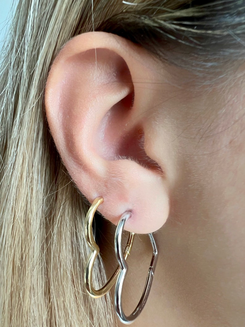 Peut inclure: Une paire de boucles d'oreilles cr&eacute;oles en forme de c&oelig;ur. Une boucle d'oreille est dor&eacute;e et l'autre est argent&eacute;e.
