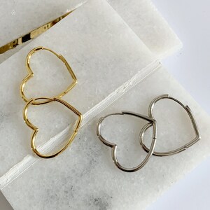 Peut inclure: Deux paires de boucles d'oreilles cr&eacute;oles en forme de c&oelig;ur, une paire est dor&eacute;e et l'autre est argent&eacute;e. Les boucles d'oreilles sont pr&eacute;sent&eacute;es sur une surface en marbre blanc.
