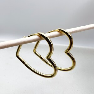 Peut inclure: Une paire de boucles d'oreilles cr&eacute;oles en forme de c&oelig;ur dor&eacute;es. Les boucles d'oreilles sont suspendues &agrave; un b&acirc;tonnet blanc.