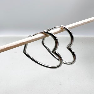 Peut inclure: Une paire de boucles d'oreilles cr&eacute;oles en forme de c&oelig;ur argent&eacute;es. Les boucles d'oreilles sont suspendues &agrave; un b&acirc;ton en bois.