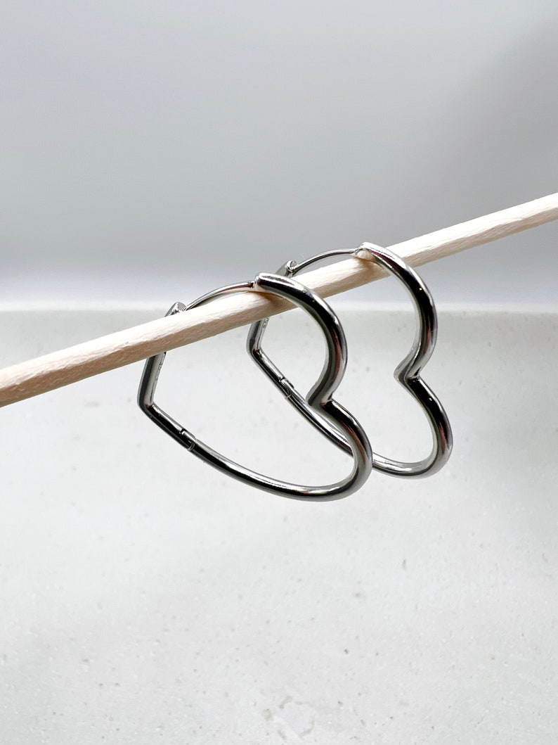 Peut inclure: Une paire de boucles d'oreilles cr&eacute;oles en forme de c&oelig;ur argent&eacute;es. Les boucles d'oreilles sont suspendues &agrave; un b&acirc;ton en bois.