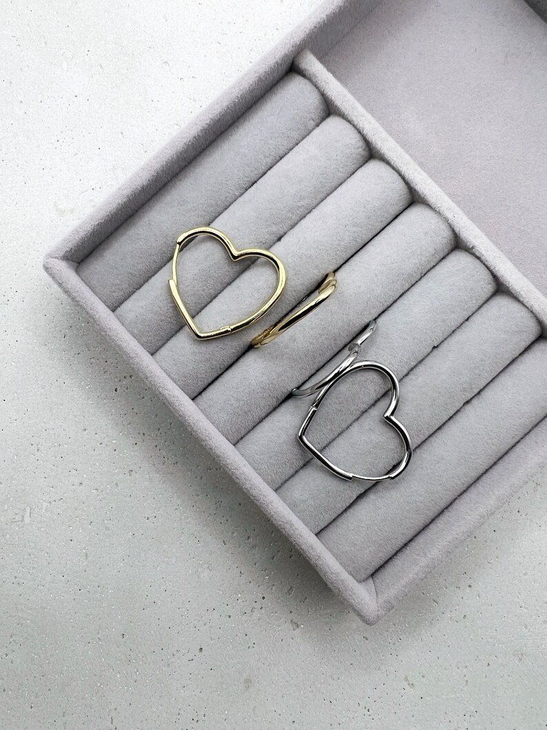 Peut inclure: Deux boucles d'oreilles cr&eacute;oles en forme de c&oelig;ur, l'une dor&eacute;e et l'autre argent&eacute;e, pr&eacute;sent&eacute;es dans un &eacute;crin &agrave; anneaux en velours gris.