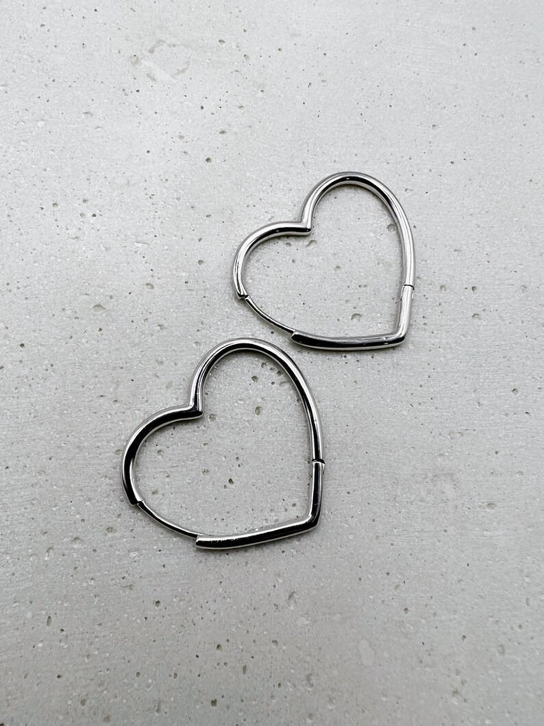 Peut inclure: Deux boucles d'oreilles cr&eacute;oles en forme de c&oelig;ur argent&eacute;es. Les boucles d'oreilles sont simples et &eacute;l&eacute;gantes.