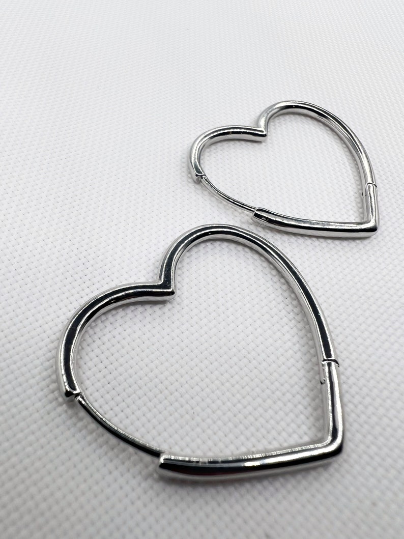Peut inclure: Deux boucles d'oreilles cr&eacute;oles en forme de c&oelig;ur argent&eacute;es. Les boucles d'oreilles sont en m&eacute;tal lisse et brillant.