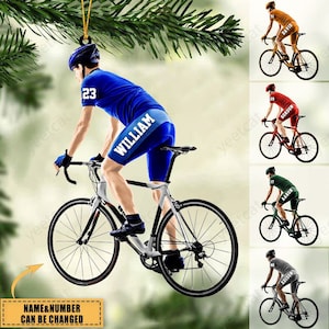 May include: A personalized Christmas ornament featuring a cyclist riding a white bicycle. The cyclist is wearing a blue jersey with the number 23 and the name "WILLIAM" on the back. The ornament is a great gift for any cyclist.
